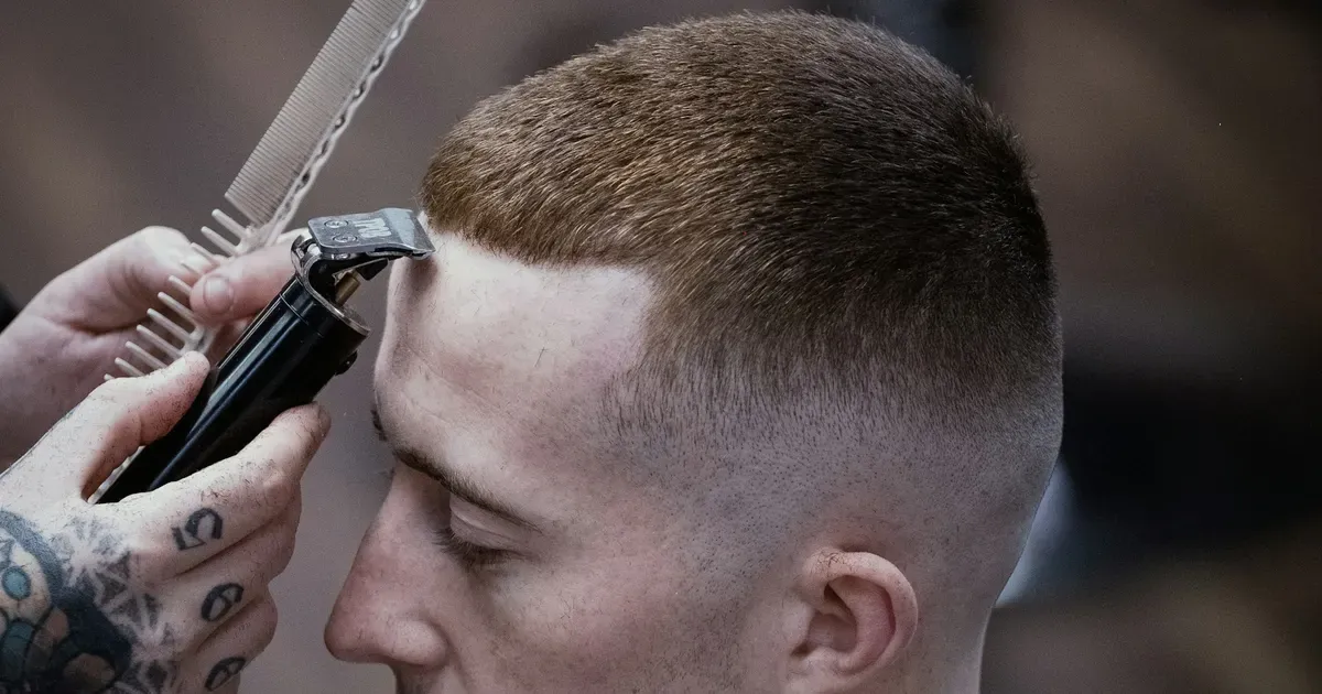 Barbeiro a fazer um corte com degradê, visto de perfil