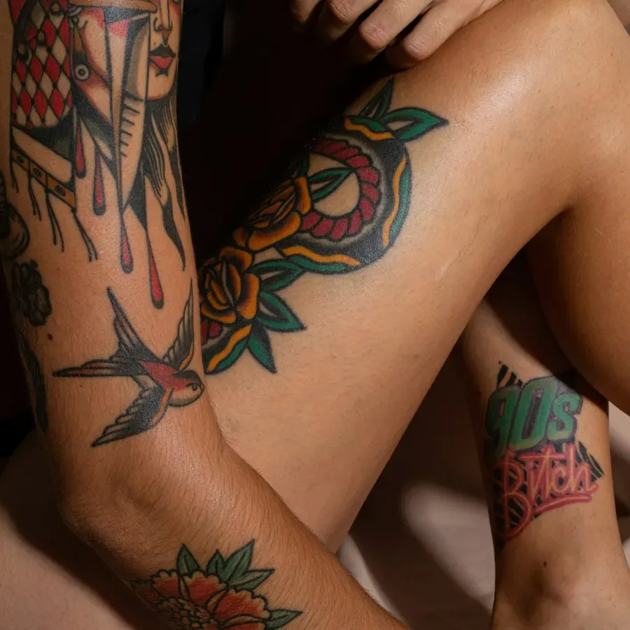 Tatuagens no estilo tradicional, com andorinhas e rosas a cores, numa perna e num braço